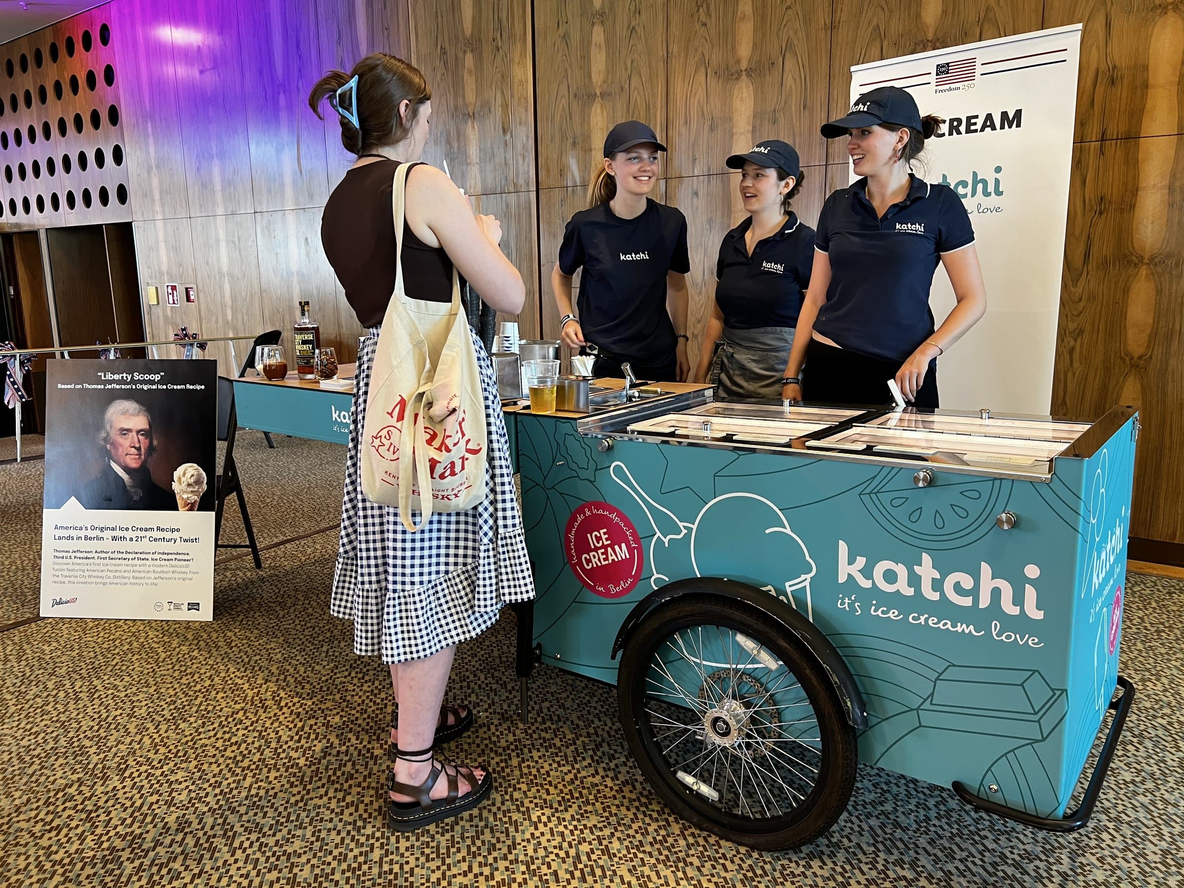 Drei Katchi-Mitarbeiterinnen in Katchi-Caps und -Shirts hinter dem türkisen Katchi Ice Cream Bike beim Event