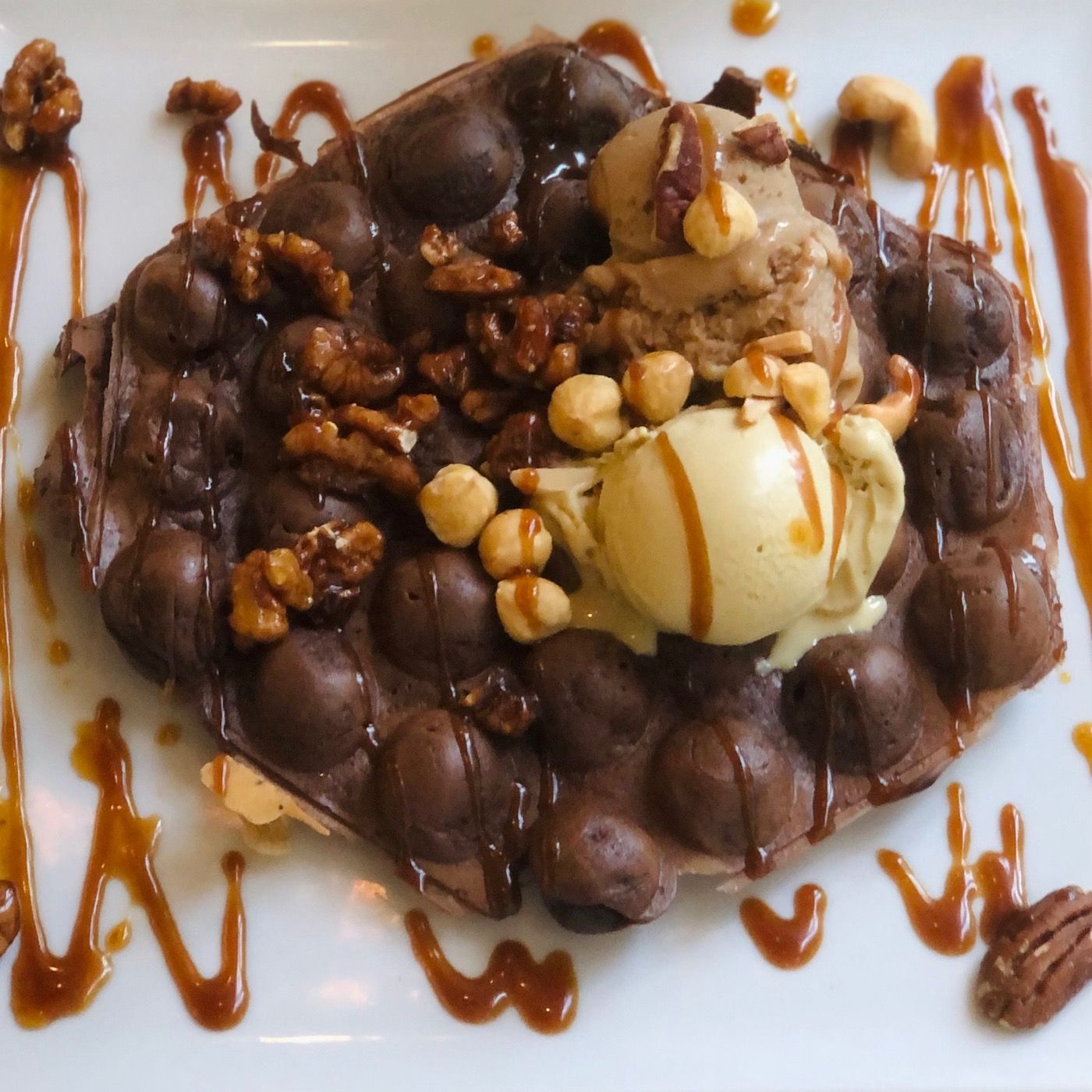 Schoko-Bubble-Waffle flach auf dem Teller mit Eis, Nüssen und Karamellsauce