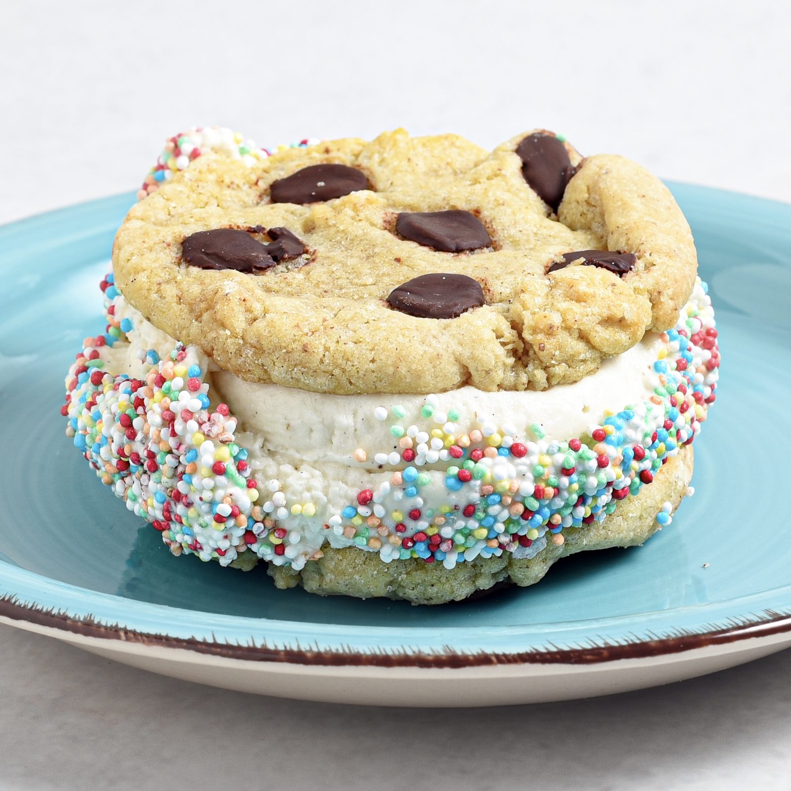 Ice Cream Sandwich mit Vanilleeis zwischen zwei Chocolate-Chip-Cookies, der Eisrand in bunten Streuseln gewälzt
