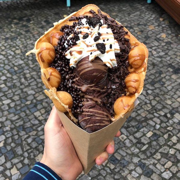 Bubble Waffle in der Hand, gefüllt mit Schokoeis, Sahne und Cookie-Crumbles