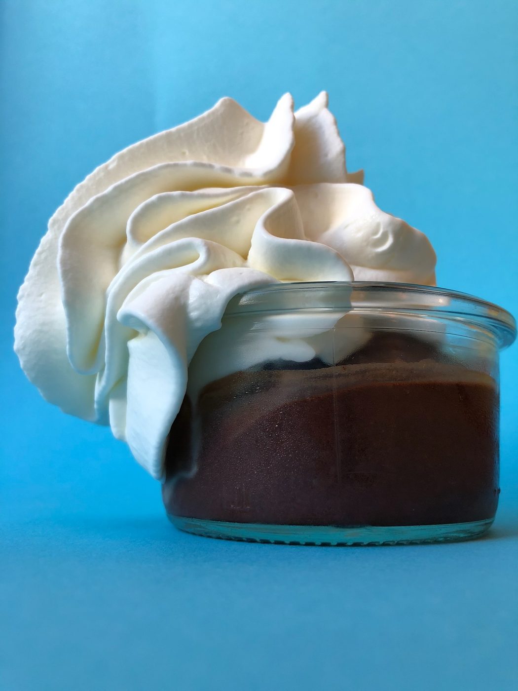Schokoladendessert im Glas mit Sahnehaube vor blauem Hintergrund