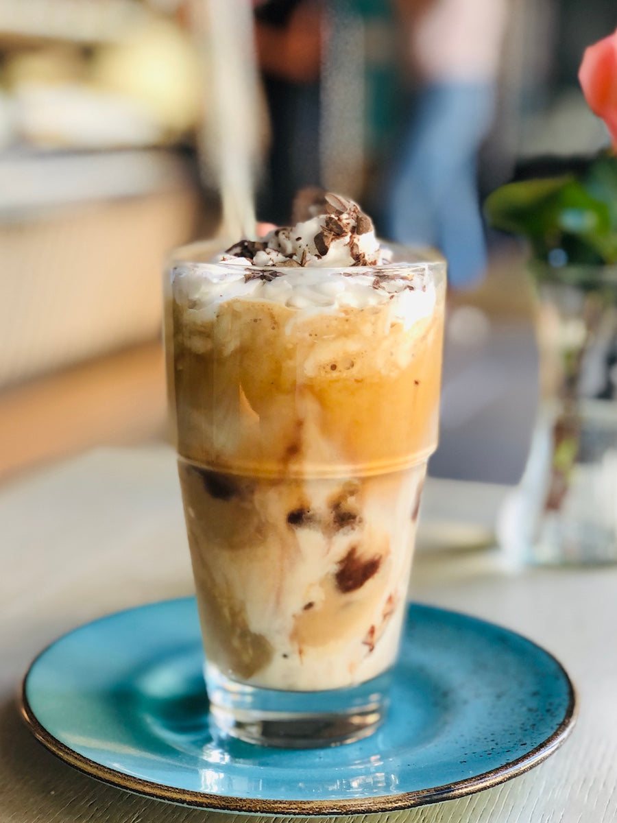 Eiskaffee im Glas mit Sahne und Schokoraspeln auf türkisem Teller