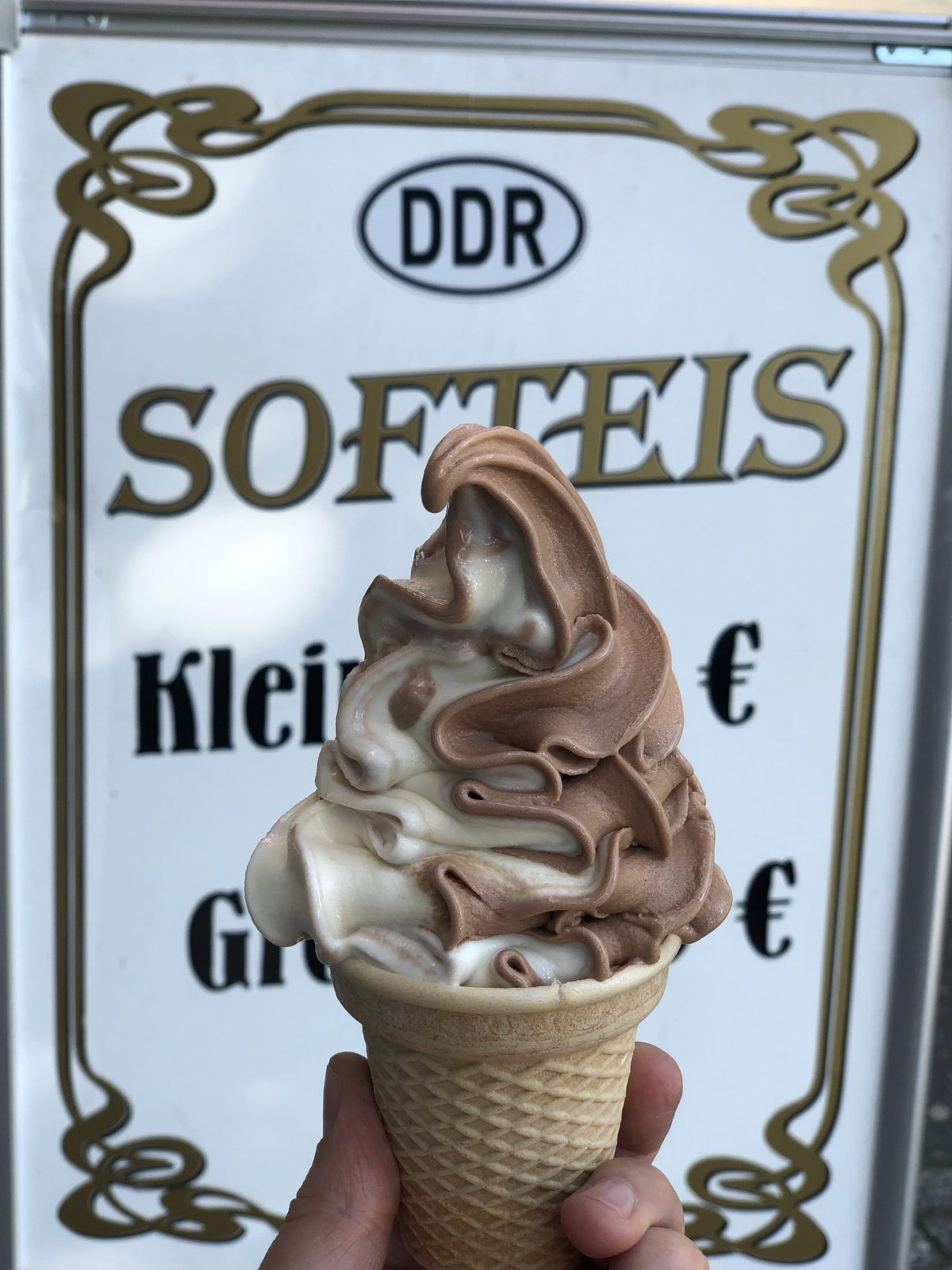Schoko-Vanille-Softeis in der Waffel vor einem Schild mit der Aufschrift DDR Softeis
