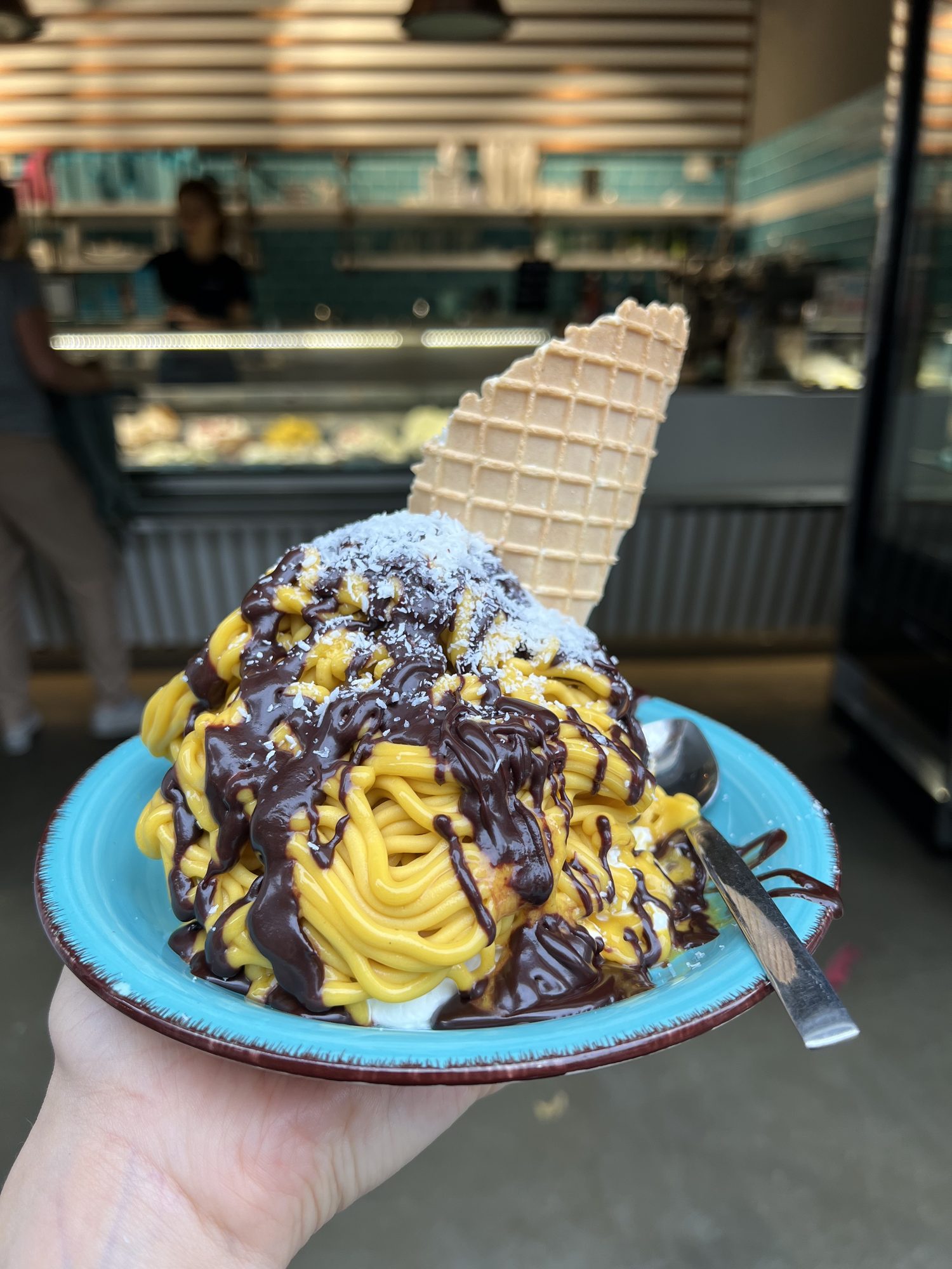Veganes Spaghettieis aus Mangosorbet mit Schokosoße und Kokosraspeln auf türkisem Teller bei Katchi