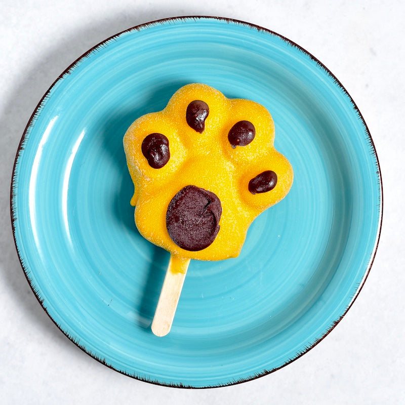 Mango-Eis am Stiel in Tatzenform auf einem türkisen Teller